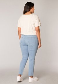 Light beige short-sleeve top and light wash skinny jeans with frayed hem. Model wears white sneakers. Simple, casual design.
