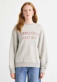 Šedá mikina s kulatým výstřihem a dlouhými rukávy. Na přední straně je červený nápis: "CONNECTICUT GANT 1949". Měkká textilní struktura.