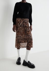 Svart stickad tröja, knälång genomskinlig kjol med brun och svart leopardprint, och kraftiga svarta loafers som bärs med vita ankelsockor.