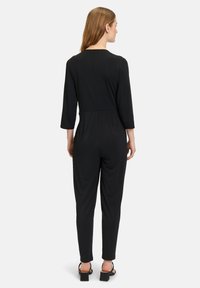 Tutina nera con maniche a tre quarti, vita aderente e gambe affusolate. Realizzata in un tessuto liscio e elastico, senza fantasie o dettagli decorativi.