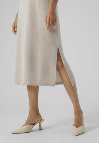 Neule, vaalea beige mekko, jossa on sivuaukko, teksturoitu kangas; yhdistettynä luonnonvalkoisiin kärjellisiin kengänsäilöihin, joissa on kolmiomainen korko.