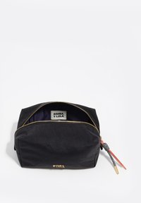 Bolsa de cosméticos de tela negra con una cremallera dorada, asa acentuada y un logotipo en la parte frontal. Cuenta con un interior forrado para organización.