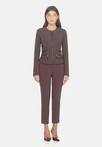 Giacca tailoring bordeaux con zip frontale e tasche laterali abbinata a pantaloni aderenti. Tessuto opaco con texture liscia e dettagli di cucitura sottili.