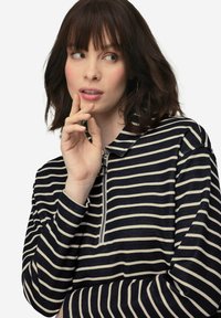 Maglia zip-up a righe blu navy e crema con colletto alla cinese, dotata di maniche lunghe e un tessuto testurizzato.