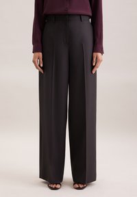 Weite Hosen aus dunkelgrauem Stoff mit flachem Frontbereich, Falten und taillierter Passform, kombiniert mit einem bordeauxfarbenen Langarmhemd.