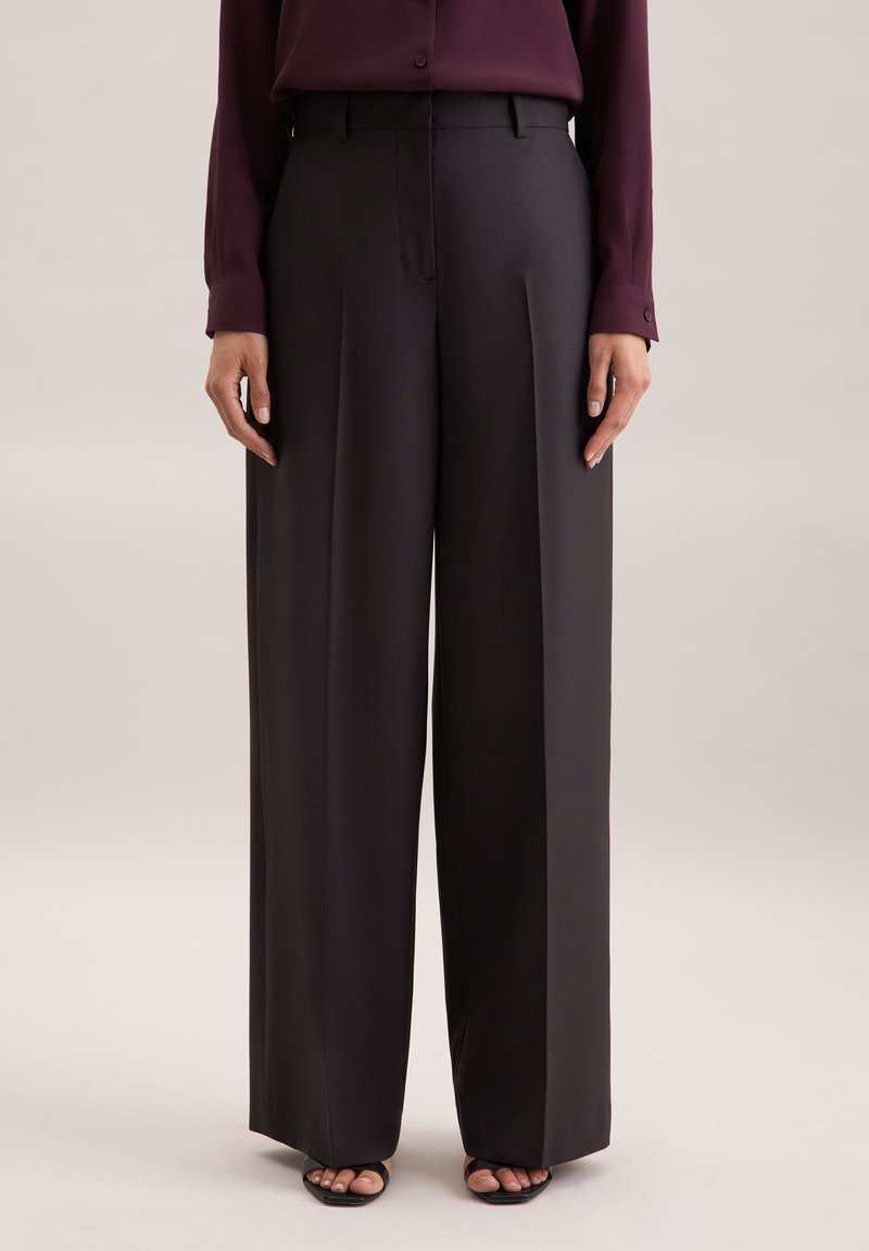 Weite Hosen aus dunkelgrauem Stoff mit flachem Frontbereich, Falten und taillierter Passform, kombiniert mit einem bordeauxfarbenen Langarmhemd.