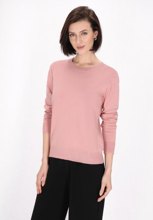 Pulover tricotat roz deschis, cu guler rotund, mâneci lungi și tiv rigelin. Asortat cu pantaloni negri cu picioare largi.