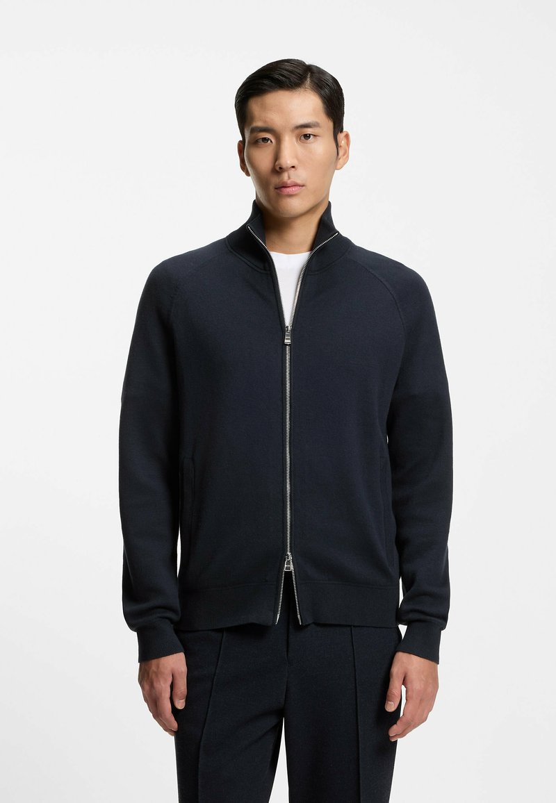 Pull à zip marine avec col montant, poignets côtelés et deux poches latérales. Tissu doux avec une texture lisse, conçu pour un look ajusté.