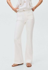 Jeans acampanados blancos de denim, con dos bolsillos traseros y una textura suave. Combinados con una blusa clara y sandalias planas.