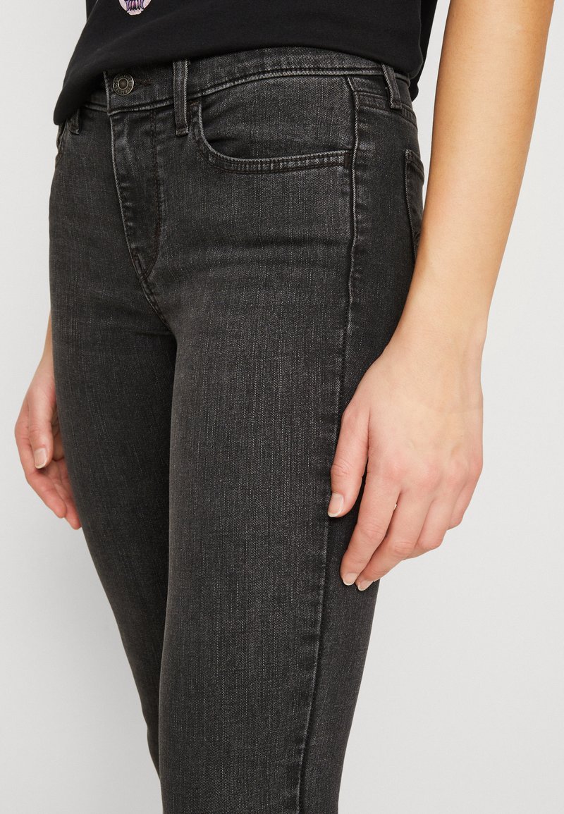 Jeans skinny negros de denim, con un diseño de cinco bolsillos, ajuste slim y un ligero desgaste. La tela tiene una textura suave con un ligero brillo.