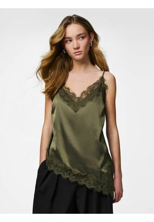 Jeune femme aux cheveux ondulés portant un caraco en satin vert olive avec une bordure en dentelle et un pantalon large noir, regardant légèrement sur le côté.