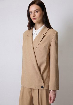 Tan blazer with a tailored design, single-button closure, notch lapels, and two front pockets, paired with a white collared shirt.