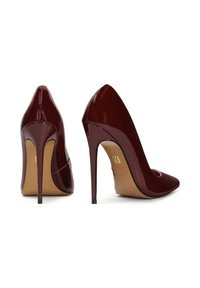 Para błyszczących, ciemnoczerwonych czółenek na wysokim obcasie, z ostrymi czubkami, obcasami typu stiletto i beżowymi podeszwami, prezentowanych na białym tle.