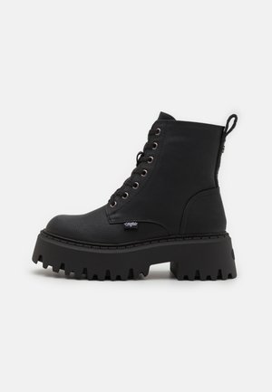 Bottine noire avec bout arrondi, tige en cuir synthétique texturé, semelle plateforme robuste, laçage à l'avant et languette à l'arrière.