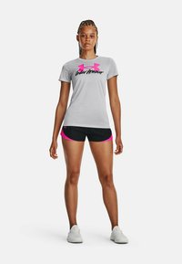 Camisa gris de manga corta con logo rosa, combinada con pantalones cortos negros con acentos rosas. Zapatillas deportivas blancas completan el atuendo.