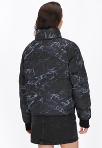 Zwarte pufferjack met een marmerpatroon in blauwtinten. Voorzien van een hoge kraag en elastische manchetten voor warmte en comfort.