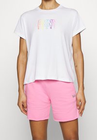 White short-sleeve t-shirt with a multicolored "DKNY SPORT" logo, paired with pink shorts featuring embroidered branding.