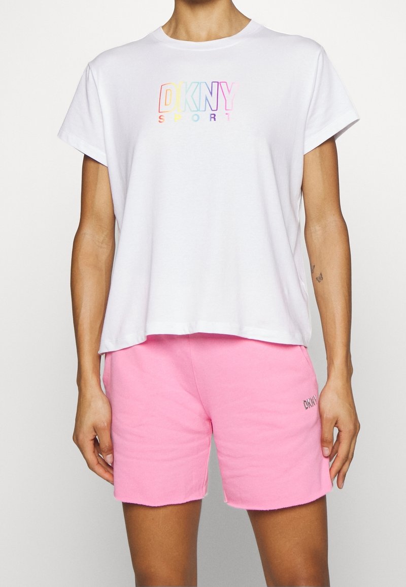 White short-sleeve t-shirt with a multicolored "DKNY SPORT" logo, paired with pink shorts featuring embroidered branding.