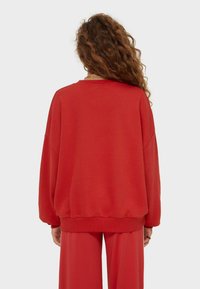 Rode oversized sweatshirt met een geribbelde zoom en manchetten, gemaakt van zachte stof. Heeft een ontspannen pasvorm en brede mouwen, met zicht op de achterkant.