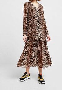 Leopardenmuster, langärmliges Kleid mit Wickeldesign, Rüschensaum und einem Taillengürtel, kombiniert mit klobigen Turnschuhen in einem mehrfarbigen Design.