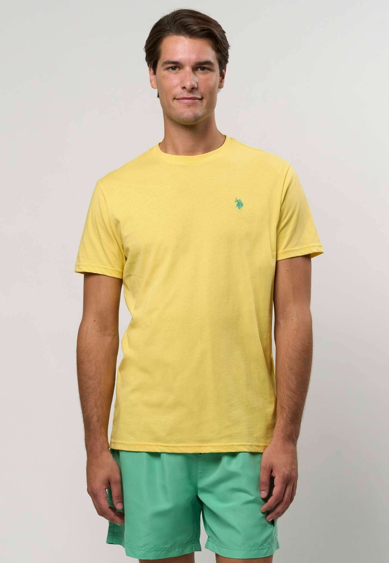Żółta bawełniana koszulka z okrągłym dekoltem i małym turkusowym logo na piersi, zestawiona z miętowymi szortami.