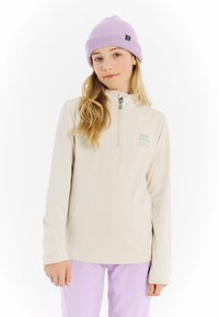 Lichtbeige ritsjack met een hoge kraag en turquoise logo-details. Gecombineerd met roze-paarse broek en een lavendelgebreide beanie.