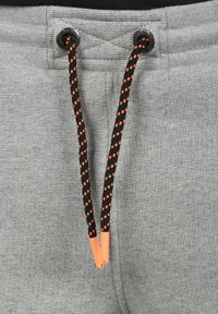 Grijze sweatpants met een gestructureerde afwerking, voorzien van een trekkoord met zwart en oranje patroonaccenten en plastic uiteinden.