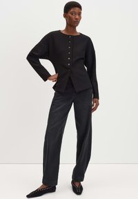 Top nero a maniche lunghe con scollatura rotonda, bottoni frontali e vestibilità rilassata. Abbinato a jeans scuri a vita alta e ballerine nere a punta.