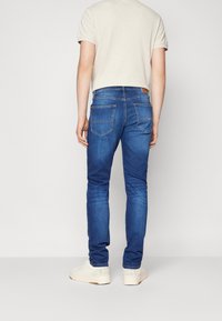 Blå denimjeans med slim fit, med bakfickor, subtila sömdetaljer och en läderlapp vid midjebandet. Stylad med vita sneakers.