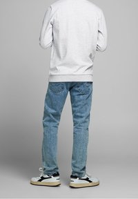 Felpa grigia, jeans azzurri, sneakers bianchi e neri. Texture denim visibile, polsini a coste e dettagli della tasca posteriore.