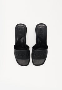 Črne DKNY natikače imajo teksturirano zgornjost z blagovno znamko na traku, gladko podplato in zaobljen prst. Oblika vključuje minimalističen stil.