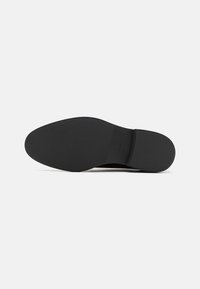 Semelle de chaussure noire avec motifs texturés antidérapants à l'avant et au talon, présentée sur un fond blanc uni.