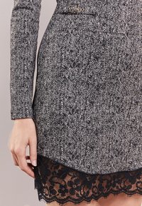 Robe à motif chevron noir et blanc avec des manches longues et un ourlet en dentelle. Présente un léger éclat et un détail en boucle métallique.
