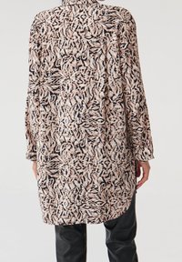Camicia lunga e ampia con motivo floreale, caratterizzata da tonalità di nero, crema e rosa chiaro. Texture morbida e design con bottoni.