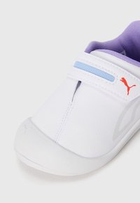 Biele tenisky Puma s fialovým vnútorným podšívkou, svetlomodrými sieťovanými detailmi, červeným logom Puma na suchom zipsu a bielou gumovou podrážkou.