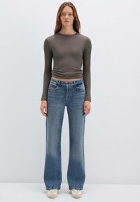 Maglia grigia a maniche lunghe a costine e jeans in denim blu a gamba larga. I jeans presentano un classico design a cinque tasche e una finitura sbiadita.