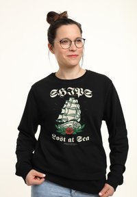 Felpa nera con stampa grafica di una nave e una rosa, con la scritta "Perso in mare". Collo a giro, maniche lunghe e texture morbida.