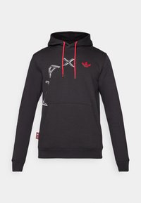 Svart hoodies med röda snoddar. Har en framträdande vit logotypdesign på framsidan och en ficka vid midjan.