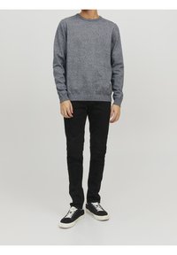 Pull gris en maille à col rond avec une finition texturée, associé à un pantalon noir slim et des baskets noires avec des accents blancs.