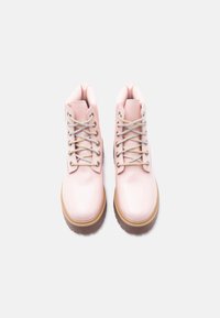 Ζεύγος στιλπνών ροζ ανοιχτόχρωμων μποτών με κορδόνια και χοντρές καφέ σόλες σε λευκό φόντο, από ψηλά.