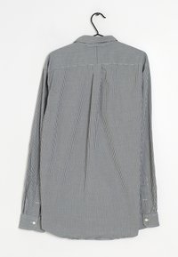 Camisa de manga larga con patrón de cuadros vichy en blanco y negro, de algodón, con cuello clásico y puños con botones, colgada de un gancho.