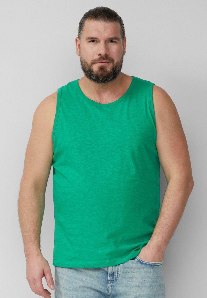 Zielony bezrękawnik z bawełny z okrągłym dekoltem, charakteryzujący się subtelną teksturą. Połączony z jasnoniebieskimi dżinsami.