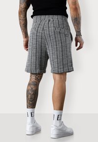 Grau und schwarz gestreifte Shorts mit lockerem Schnitt, mit umgeschlagenen Säumen und Gesäßtaschen, kombiniert mit weißen Sneakern und Socken.