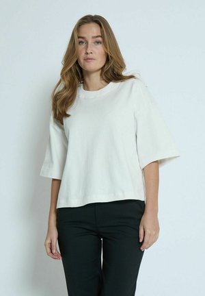 T-shirt bianca a maniche corte in morbido cotone, con vestibilità rilassata e colletto a giro, abbinata a pantaloni neri.