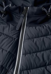 Giacca puffer navy con texture trapuntata, zip bianca a contrasto e cappuccio con cordoncino. Il materiale sembra morbido e leggero.