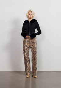 Juodas raukšlėtas užtrauktuku susegamas švarkas su dirbtinio kailio apykakle ir rankogaliais, derinamas su smėlio ir rudos leopardų rašto plačiomis kelnėmis. Aksesuarai - smėlio spalvos aukštakulniai.