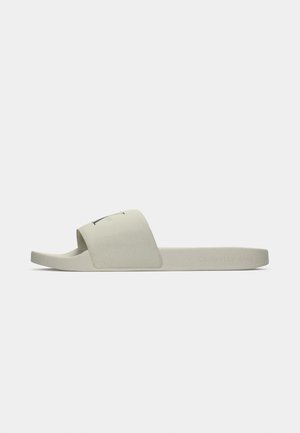 Lys grå slip-on sandaler med en glatt, matt overflate. Bred stropp med logo, konturert såle og flat såledesign.