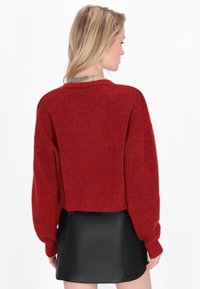 Roter, kurz geschnittener Pullover mit einer weichen, flauschigen Textur und langen Ärmeln. Kombiniert mit einem schwarzen Leder-Minirock für den Kontrast.