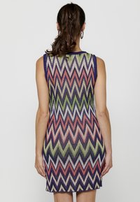 Rochie fără mâneci, ajustată, cu un model zigzag colorat în nuanțe de purpuriu, corai, verde și crem. Material tricotat texturat, de lungime până la mijlocul coapselor.