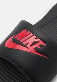 Črne škornje z drsnikom z teksturiranim črnim podplatom. Imajo širok črn trak z dvignjenim rdečim logotipom "NIKE" in rdečim znakom. 